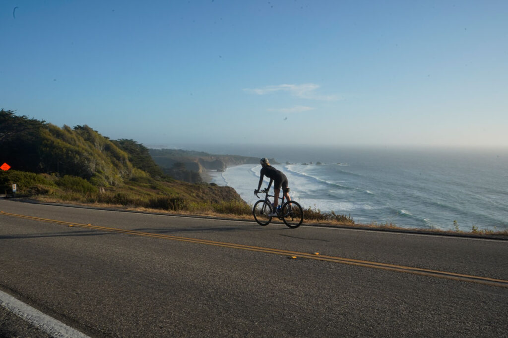 Cyclist riding along a coastal road with the ocean in the background.