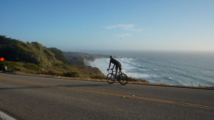 Cyclist riding along a coastal road with the ocean in the background.